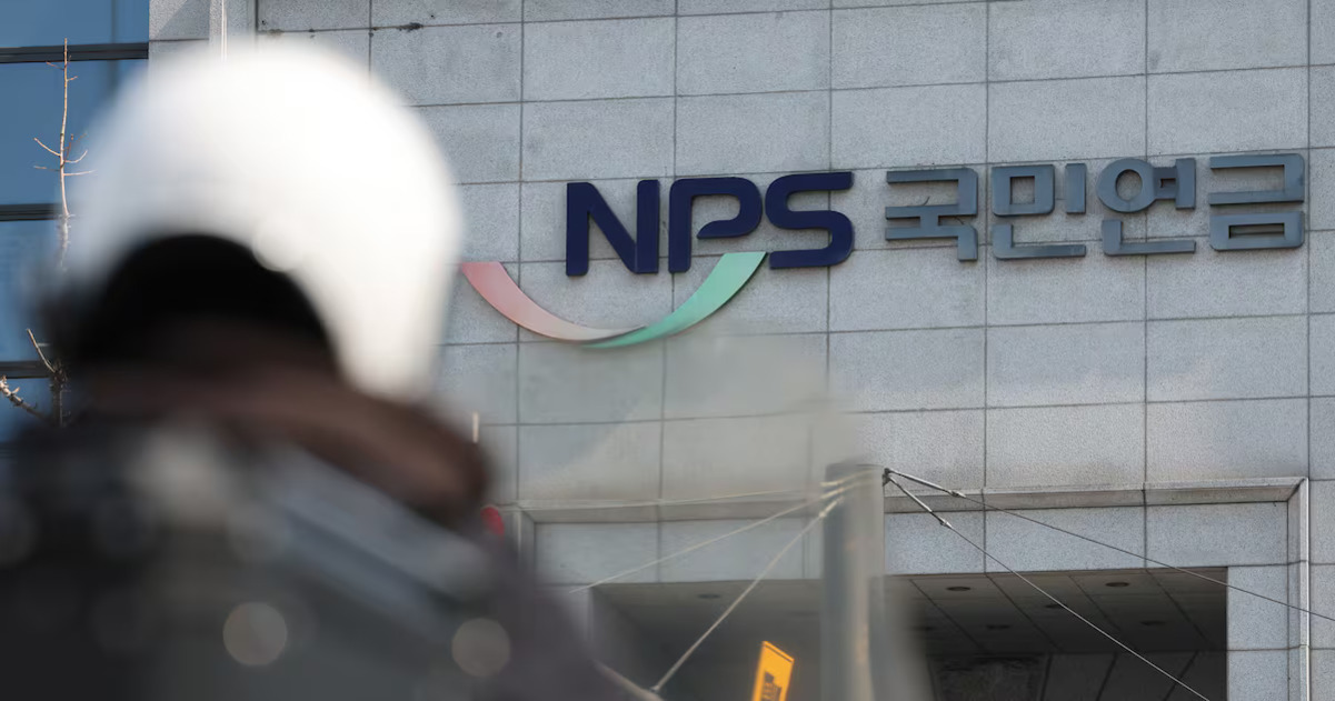 회색 건물 외벽에 'NPS 국민연금' 로고가 보이고, 앞에는 헬멧을 쓴 사람이 흐릿하게 보인다.