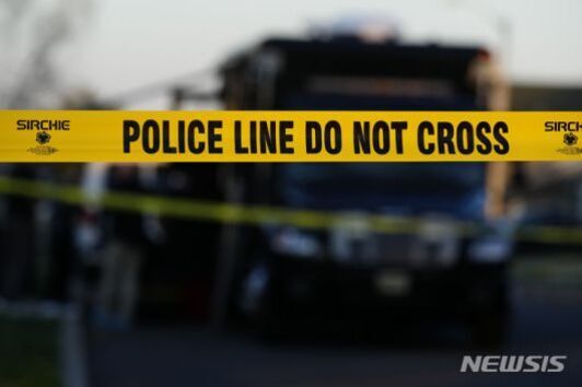 'POLICE LINE DO NOT CROSS'라고 적힌 노란색 폴리스 라인이 사건 현장을 차단하고 있으며, 배경에는 경찰 차량이 흐릿하게 보인다.