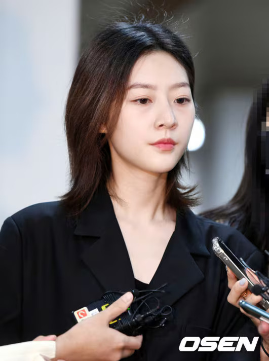검은색 옷을 입은 젊은 여성이 기자들의 마이크와 녹음기 앞에 서 있는 모습