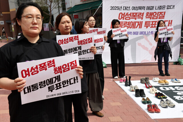여성들이 '여성폭력 책임질 대통령에게 투표한다'라는 문구가 적힌 팻말을 들고 시위하고 있으며, 바닥에는 여러 켤레의 신발이 놓여 있다. 뒤쪽 배너에도 같은 메시지가 크게 쓰여 있다.