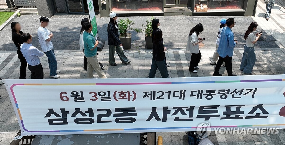 여러 명의 사람들이 야외에 설치된 '6월 3일(화) 제21대 대통령선거 삼성2동 사전투표소'라는 현수막 앞에서 줄을 서서 기다리고 있다.