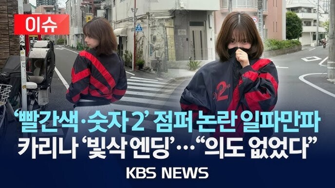 한 여성이 빨간색과 검은색이 조합된 점퍼를 입고 거리에서 포즈를 취하고 있다. 화면 하단에는 '빨간색·숫자 2' 점퍼 논란 일파만파, 카리나 '빛삭엔딩'... 의도 없었다 KBS NEWS라는 뉴스 자막이 보인다.