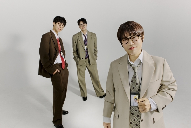 세 명의 남성이 넓은 흰색 배경에서 정장을 입고 포즈를 취하고 있다. 모두 안경을 썼으며, 신분증 목걸이를 착용했다.