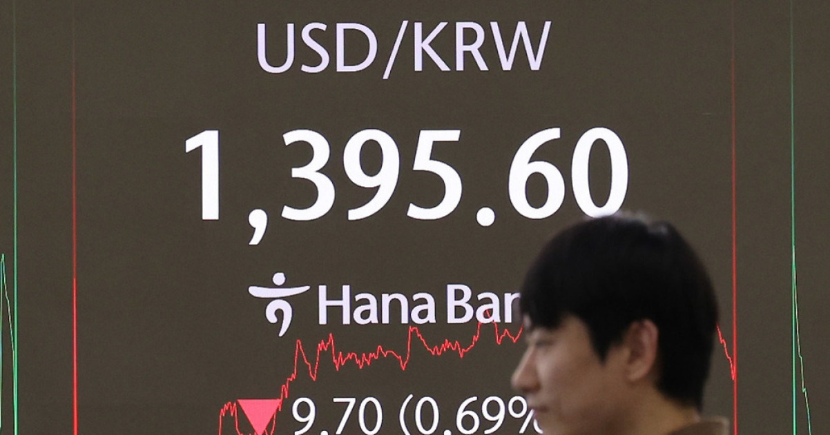 한 남성이 지나가는 가운데, 배경에는 USD/KRW 환율이 1,395.60으로 표시된 전광판이 보인다. 하단에는 하나은행 로고와 함께 변동 그래프 및 -9.70(-0.69%) 수치가 나타나 있다.