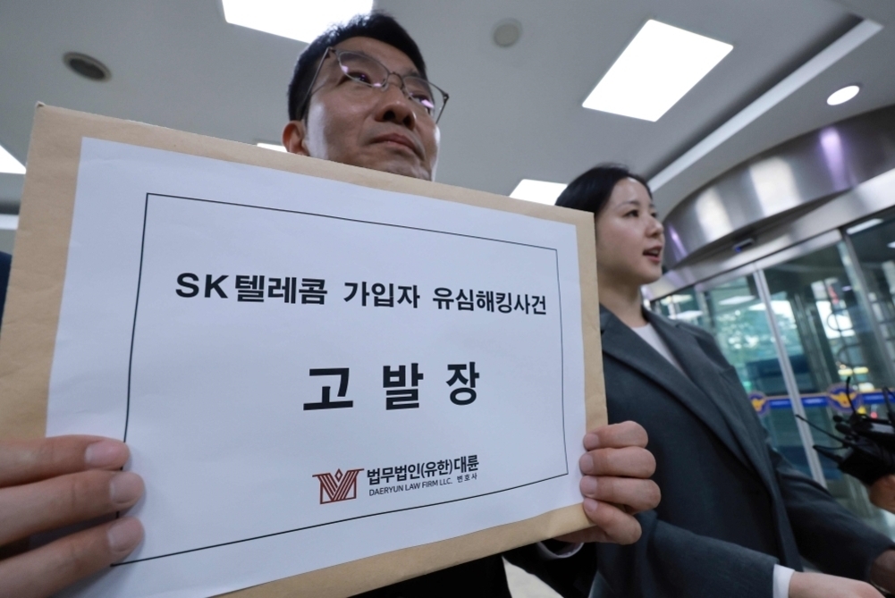 한 남성이 'SK텔레콤 가입자 유심해킹사건 고발장'이라고 적힌 서류봉투를 들고 있고, 옆에 한 여성이 함께 있는 모습
