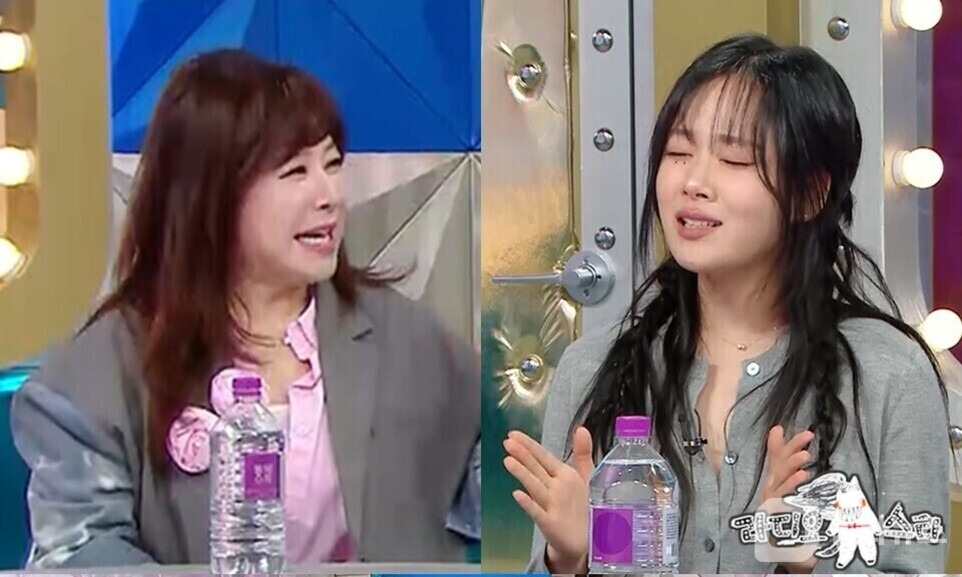 두 명의 여성이 방송 스튜디오에서 대화를 나누고 있다. 테이블 위에 생수병이 놓여 있으며, 한 여성은 웃으며 상대를 바라보고 있고 다른 여성은 눈을 감고 손짓하고 있다.