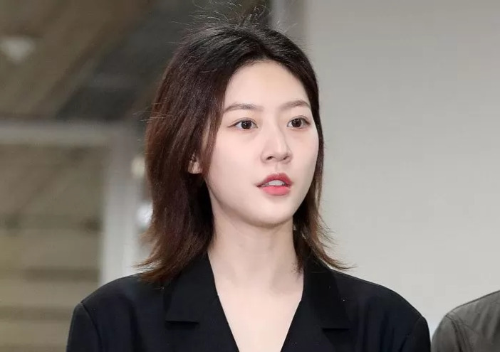 검은색 상의를 입은 젊은 여성이 실내에서 정면을 바라보고 있다.