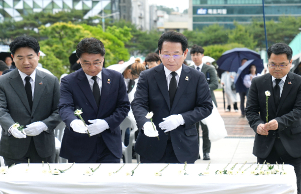 정장 차림의 남성들이 흰 장갑을 끼고 하얀 국화를 헌화하는 추모 행사 모습