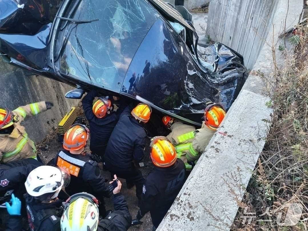 여러 명의 소방관들이 심하게 파손된 검은색 차량에서 구조 작업을 하고 있는 모습