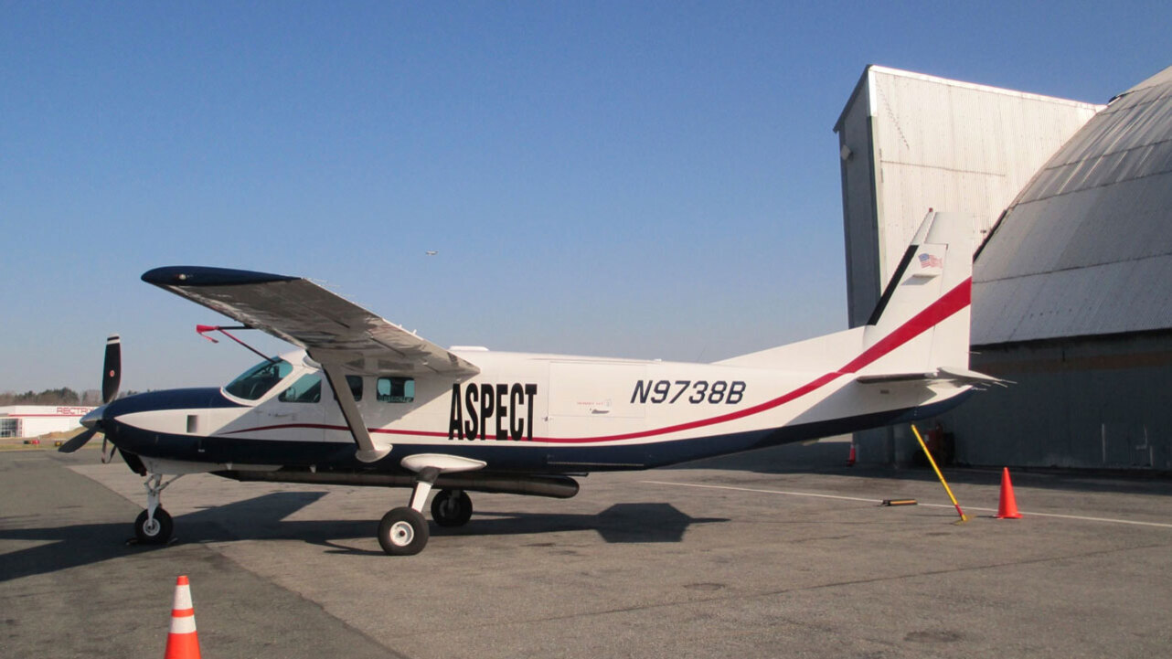 공항 활주로에 주차된 흰색과 남색의 소형 비행기, 기체에는 'ASPECT'와 등록번호 'N9738B'가 적혀 있다.