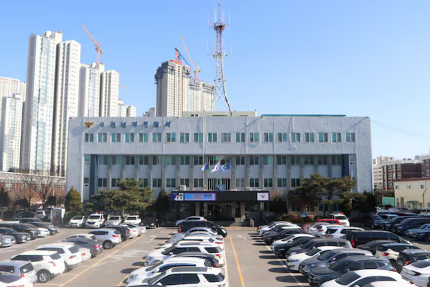 여러 대의 차량이 주차된 넓은 주차장 앞에 위치한 4층짜리 경찰서 건물, 뒤로 고층 아파트와 크레인이 보임.