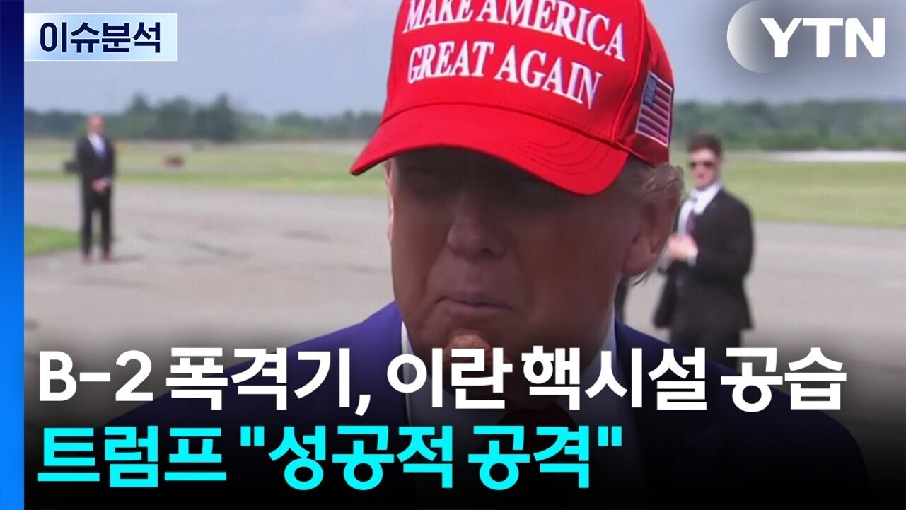 붉은색 'MAKE AMERICA GREAT AGAIN' 모자를 쓴 남성이 공항 활주로에서 인터뷰를 하고 있으며, 화면 왼쪽 상단에는 '이슈분석', 오른쪽 상단에는 YTN 로고가 있고, 하단에 한글 자막으로 'B-2 폭격기, 이란 핵시설 공습 트럼프 성공적 공격'이라는 텍스트가 있다.