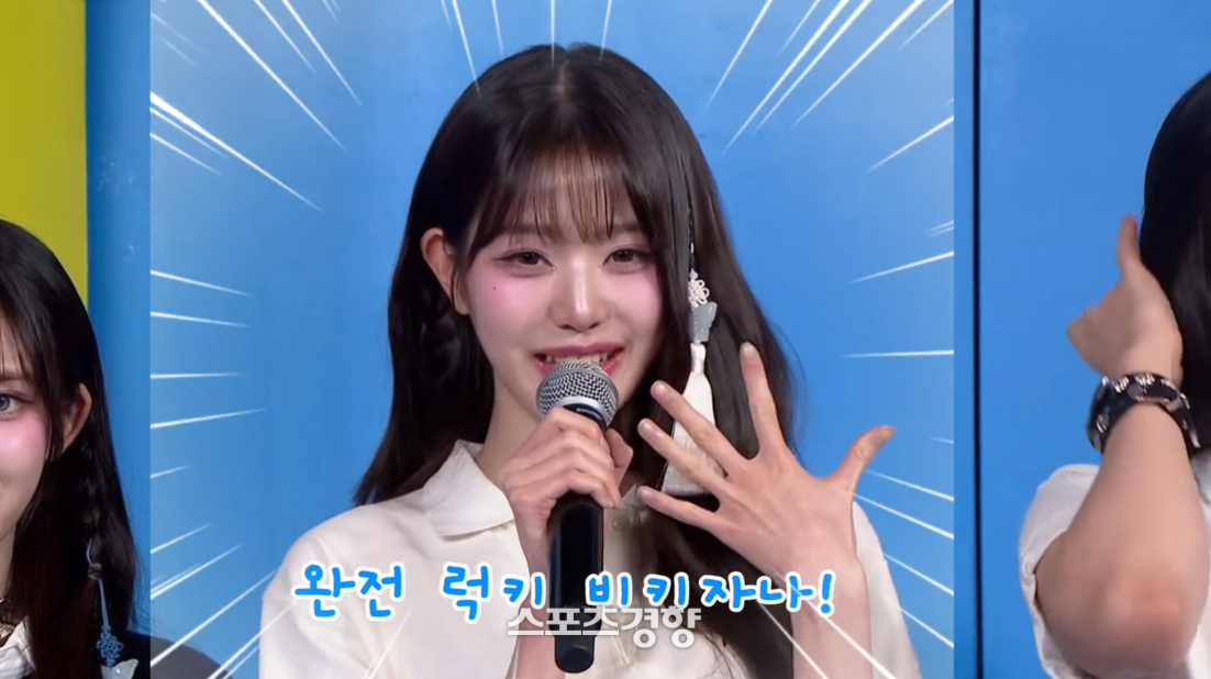 마이크를 들고 있는 젊은 여성이 손을 펴서 보여주며 미소 짓고 있다. 파란 배경과 함께 화면에는 '완전 럭키 비키잖아!'라는 자막이 보인다.