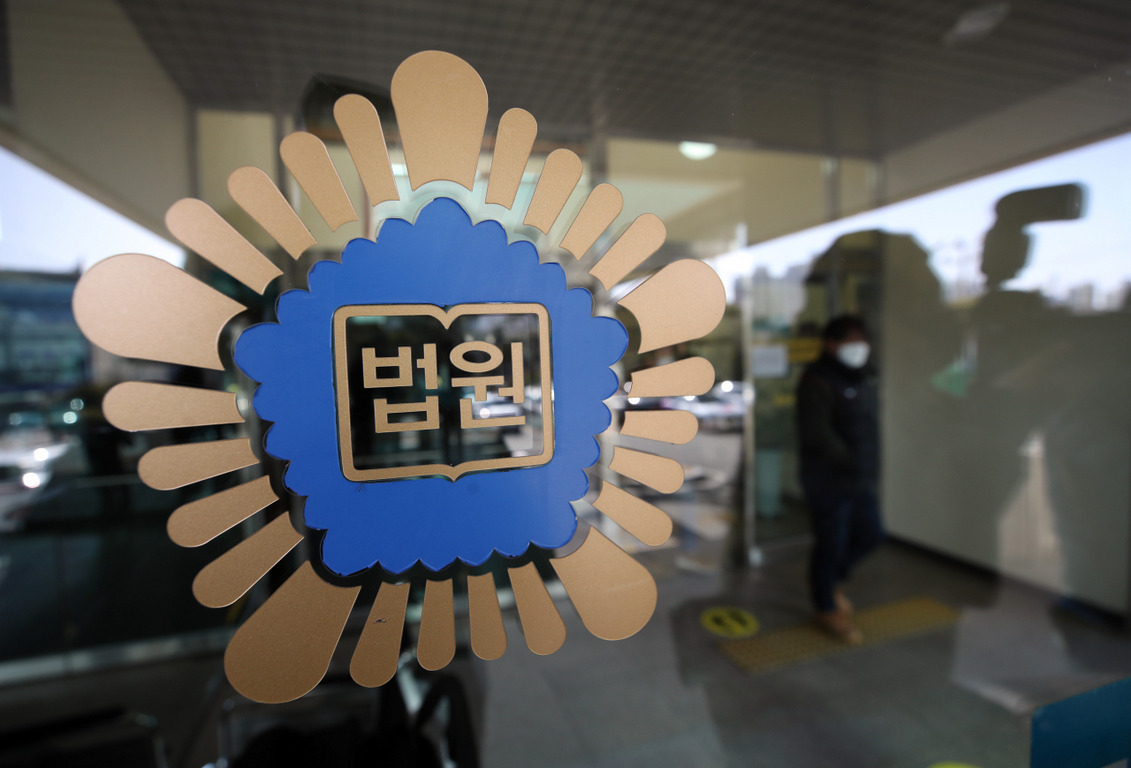 법원 마크가 붙어 있는 유리문과 그 뒤로 입구에 서있는 사람의 모습