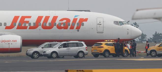 공항 활주로에 정차한 제주항공 비행기 앞에 여러 대의 차량과 사람들이 모여 있는 모습
