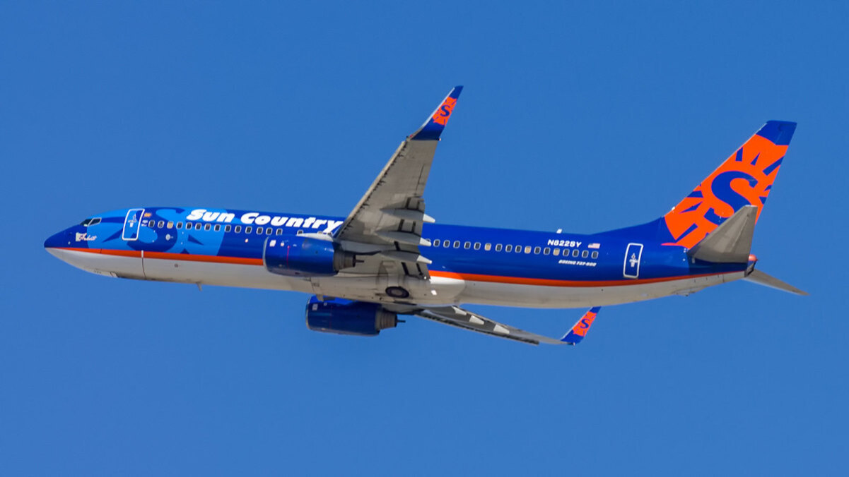 파란색과 주황색으로 도장된 Sun Country Airlines 여객기가 맑은 하늘을 비행하고 있다.