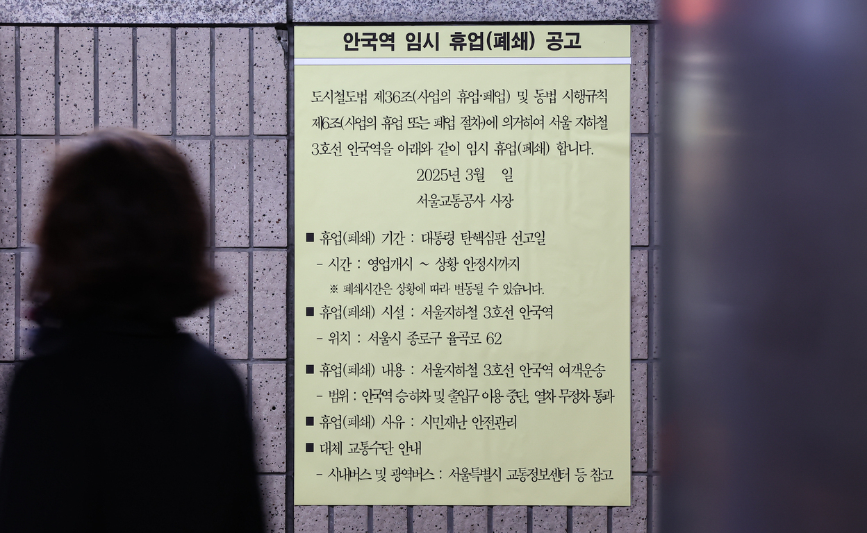 지하철 역사 벽에 '안국역 임시 휴업(폐쇄) 공고' 안내문이 붙어 있고, 한 사람이 앞을 지나가는 모습. 안내문에는 안국역의 임시 휴업 기간, 위치, 사유 등이 적혀 있다.