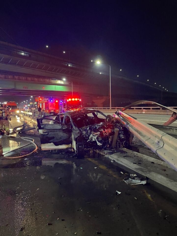 야간 고가도로 위에서 교통사고로 인해 차량이 심하게 파손되고 중앙분리대에 끼어 있으며, 주변에는 소방차와 구급차의 불빛이 비치고 구조대원이 출동해 있다.