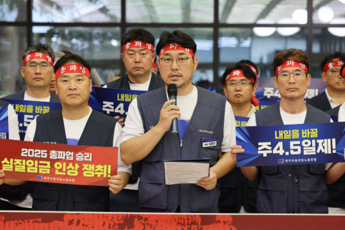 여러 명의 남성이 붉은 머리띠를 두르고 조끼를 입은 채 시위 중이며, 앞줄 인물들이 '실질임금 인상 쟁취!'와 '주 4.5일제' 등이 적힌 손팻말을 들고 있다.