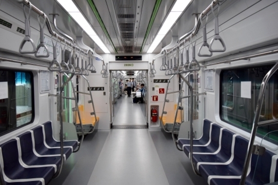 지하철 객실 내부가 텅 비어 있으며, 좌석과 손잡이가 정렬되어 있다. 멀리 몇 명의 사람이 보인다.