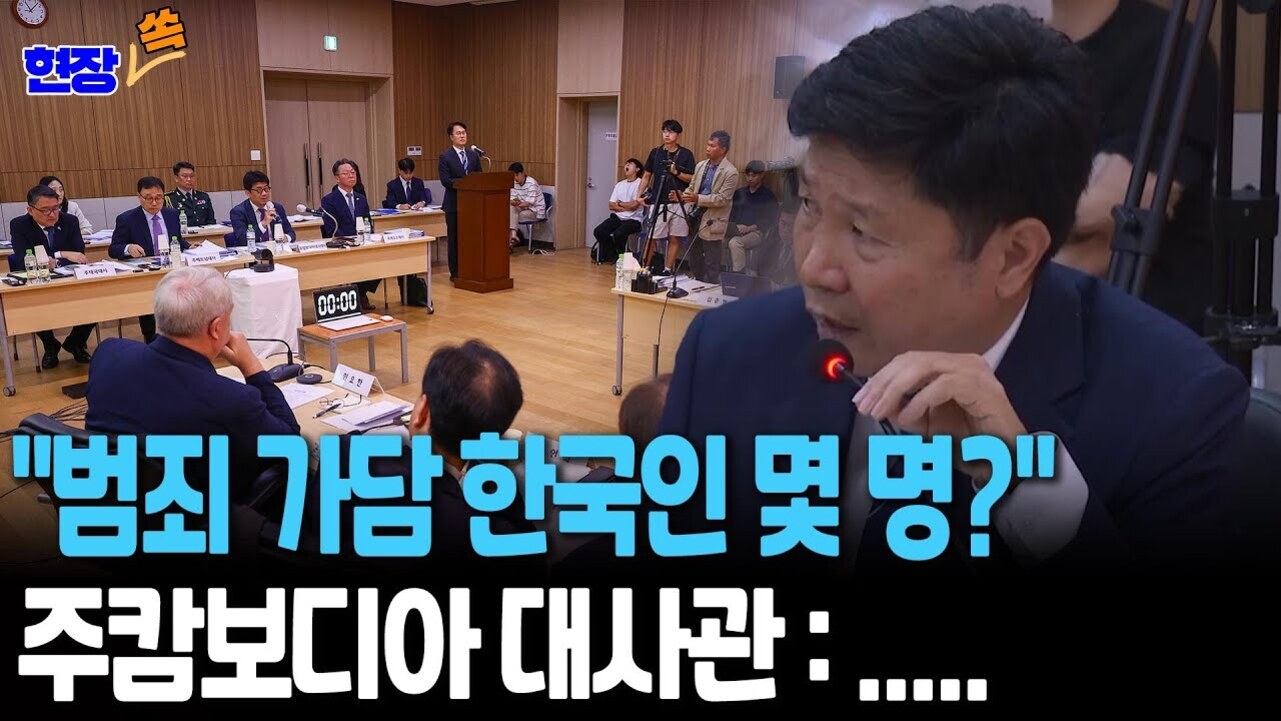 회의실에서 여러 명의 남성이 책상에 앉아 있고, 한 남성이 마이크를 들고 발언하는 모습. 화면에는 '범죄 가담 한국인 몇 명? 주캄보디아 대사관: ....'이라는 자막이 크게 표시되어 있다.