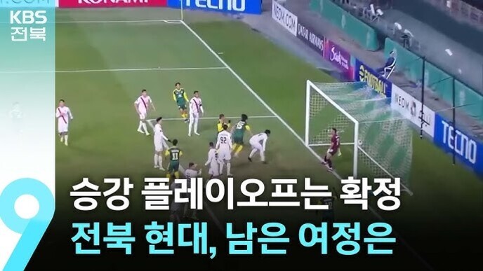 축구 경기 중 코너킥 상황에서 여러 선수들이 골문 앞에 모여 있고, 화면 하단에는 '승강 플레이오프는 확정 전북 현대, 남은 여정은'이라는 자막이 표시되어 있다.