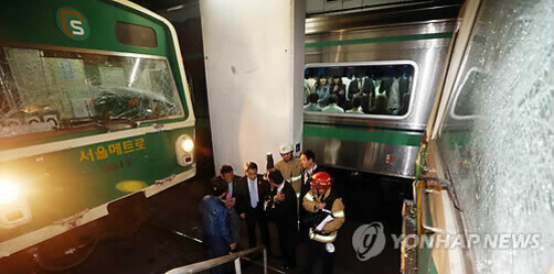 지하철 두 대가 충돌한 현장에서 유리창이 깨진 차량과 사고를 조사하는 소방관, 관계자들이 보이고, 한쪽 열차 안에는 승객들이 남아 있다.