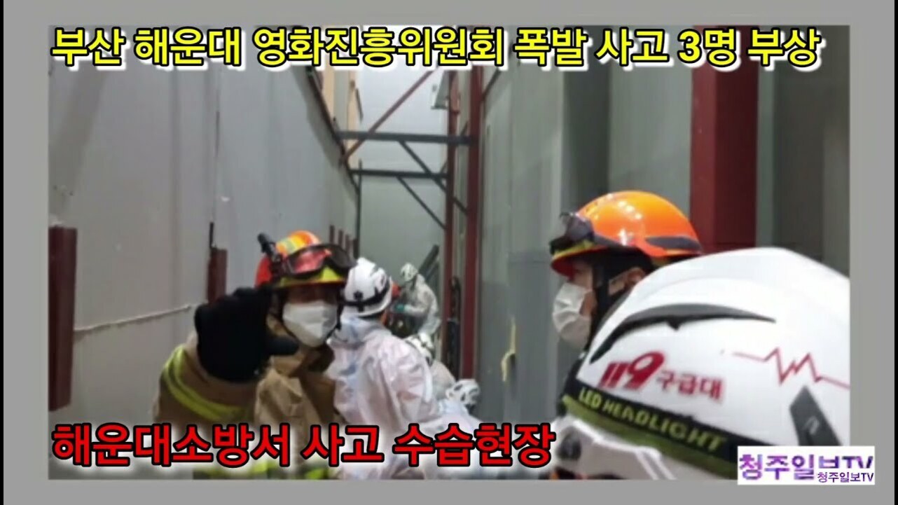 부산 해운대 영화진흥위원회에서 폭발 사고가 발생해 3명이 부상당한 현장에 소방관들과 구조대원들이 출동하여 수습 작업을 하고 있는 모습. 화면 상단에는 노란색 글씨로 사고 내용이, 하단에는 빨간색 글씨로 '해운대소방서 사고 수습현장'이라는 문구가 표시되어 있다.