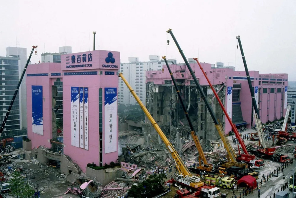 무너진 분홍색 삼풍백화점 건물과 여러 대의 크레인 및 구조 차량이 사고 현장에서 구조 작업을 하고 있는 모습