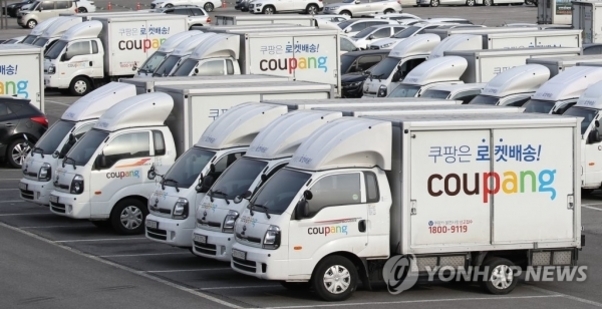 여러 대의 쿠팡 로켓배송 트럭이 주차장에 정렬되어 있다.