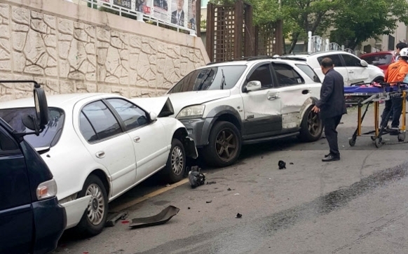 도로 위에 세 대의 차량이 연쇄적으로 추돌한 사고 현장. 한 명은 들것으로 이송되고 있으며, 남성이 사고 차량 옆에서 상황을 살피고 있다.