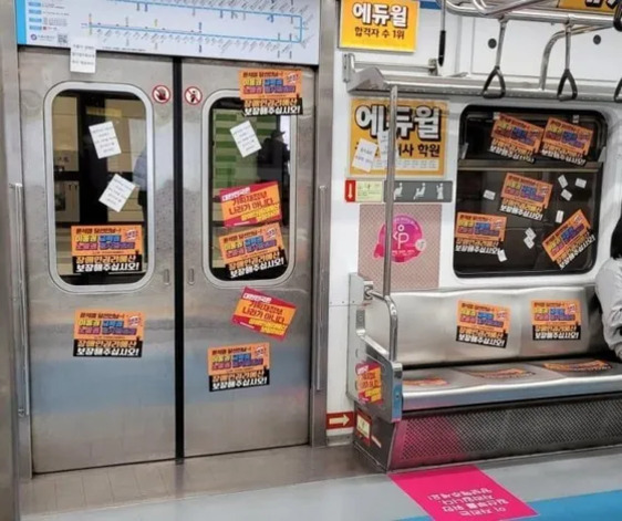 지하철 내부의 문과 벽, 좌석 등에 다양한 색상의 광고 스티커들이 많이 붙어 있는 모습. 한쪽에 승객이 앉아 있다.