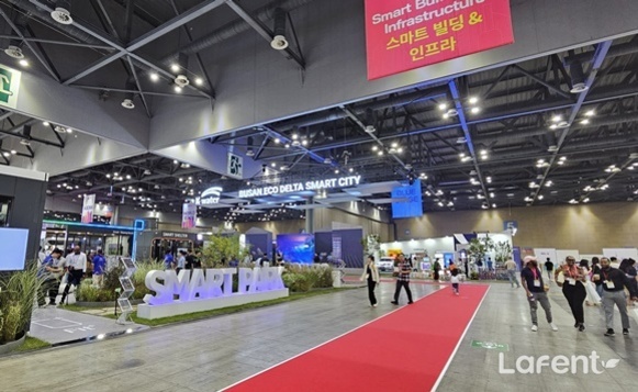 실내 전시회장에서 'SMART PARK' 조형물과 붉은 카펫이 보이며, 여러 부스와 사람들이 관람하고 있다. 천장에는 '스마트 빌딩 & 인프라'라는 현수막이 걸려있다.