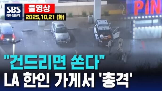 SBS 뉴스 영상 캡처로, LA 한인 가게에서 총격 사건이 발생했다는 자막과 함께 2025년 10월 21일 날짜가 표시되어 있다. 주차장에는 차들이 서 있고 경찰 차량도 보인다.