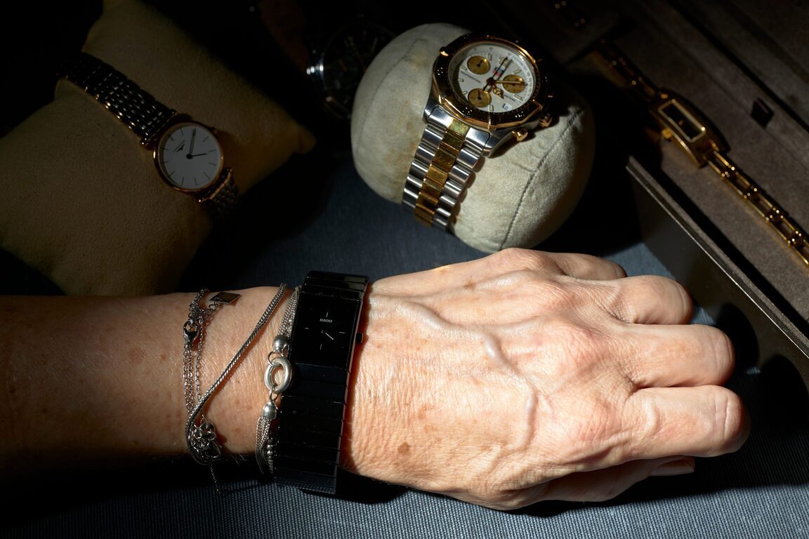 여러 개의 고급 손목시계와 팔찌가 보이며, 한 사람이 검은색 시계를 착용하고 있다. 주변에는 쿠션에 올려진 금속 밴드 시계들과 케이스 안에 정리된 시계들이 함께 놓여 있다.