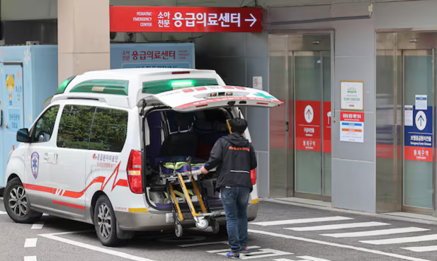 병원 응급의료센터 앞에 구급차가 정차해 있고, 한 사람이 들것을 준비하고 있는 모습.