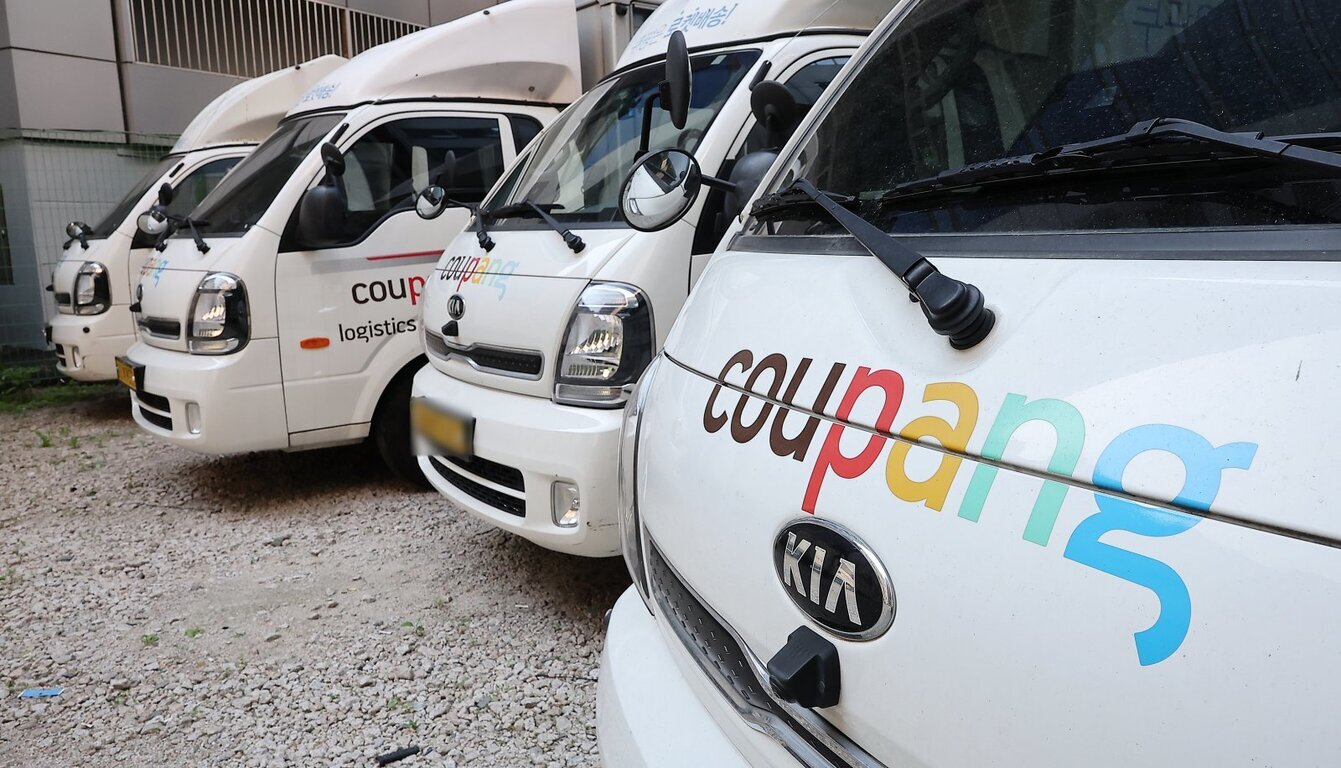 쿠팡 로고가 있는 흰색 택배 트럭 여러 대가 주차되어 있다.