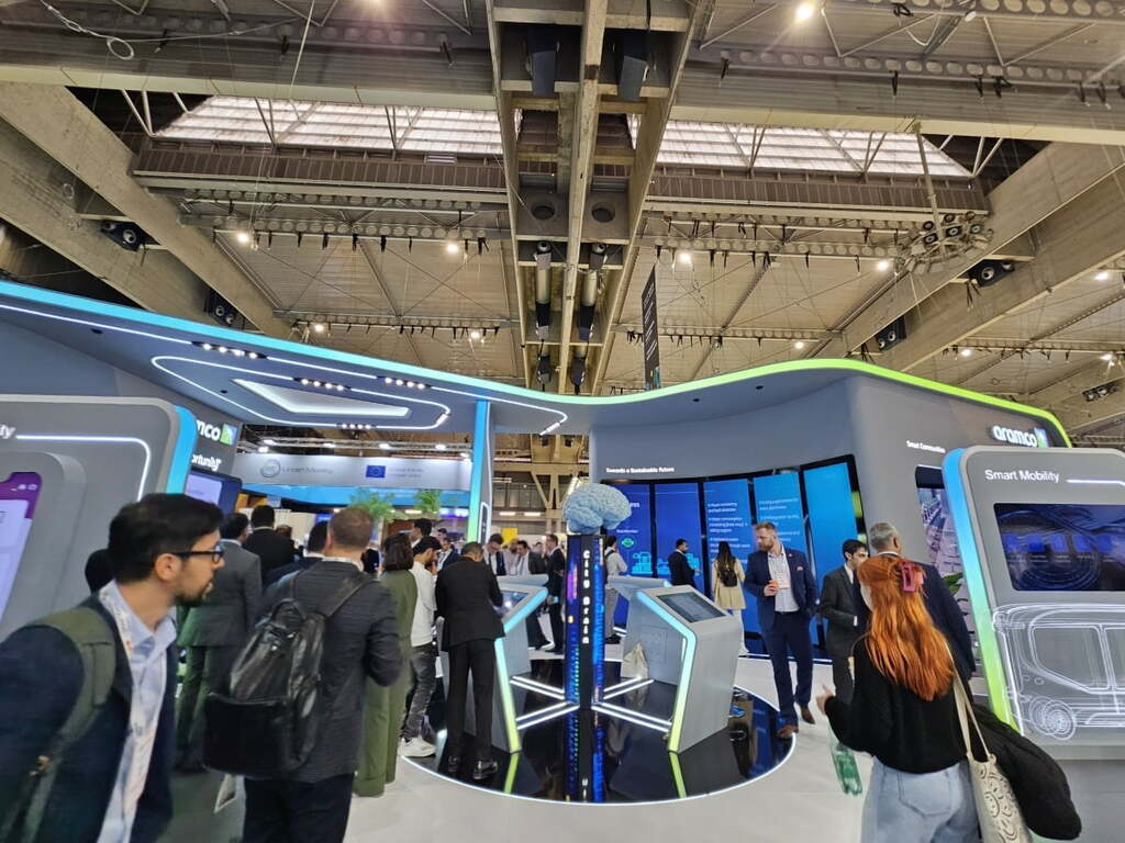 전시회장에서 여러 사람들이 부스를 둘러보고 있으며, 부스에는 디지털 스크린과 미래형 모빌리티 관련 전시물이 있다.