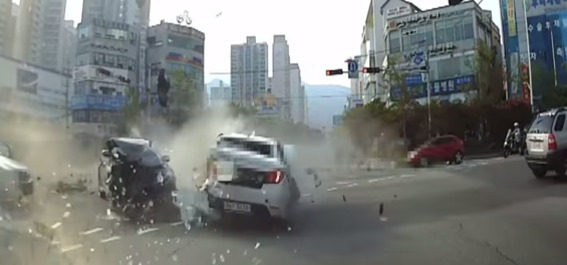 도심 교차로에서 두 대의 차량이 충돌하여 유리 파편과 연기가 발생한 사고 현장.