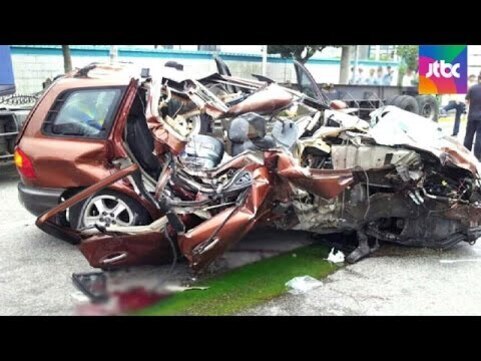 심하게 파손된 갈색 승용차가 도로 위에 멈춰 있다. 차량 전면부와 측면이 크게 부서져 형태를 알아보기 어렵다.