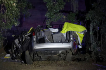 나무와 흙 위에 심하게 파손된 자동차 한 대가 밤에 놓여 있다. 차량 윗부분에는 노란색 천이 덮여 있다.